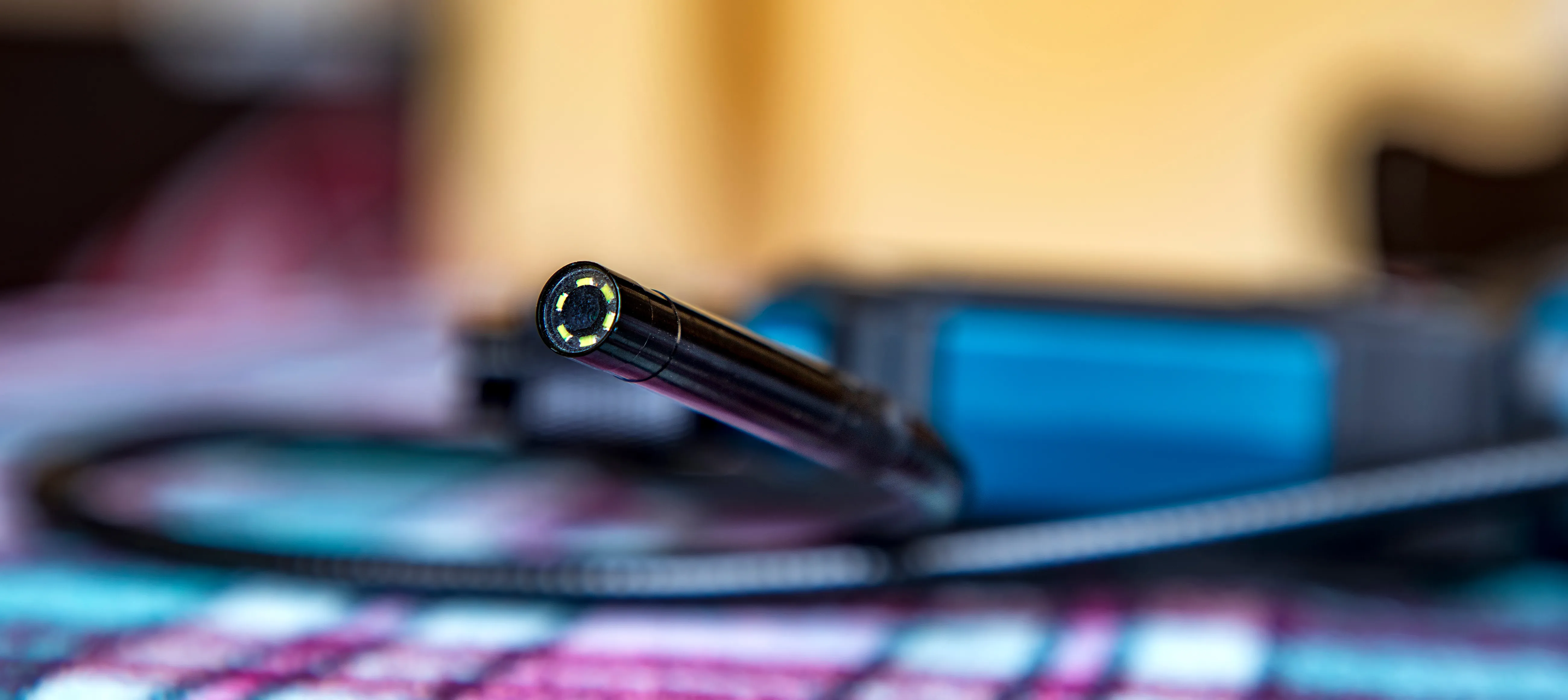 A close up of a clean drain scope camera with its lens facing the viewer and its cable coiled behind.