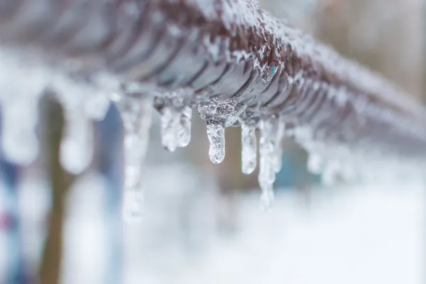 A frozen pipe with shimmering icicles melting and dripping.