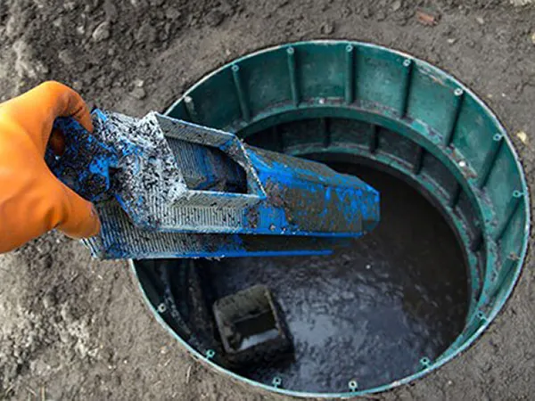 A hand with a bright yellow glove on lifts a component out of a septic tank, checking to ensure it is in working condition.