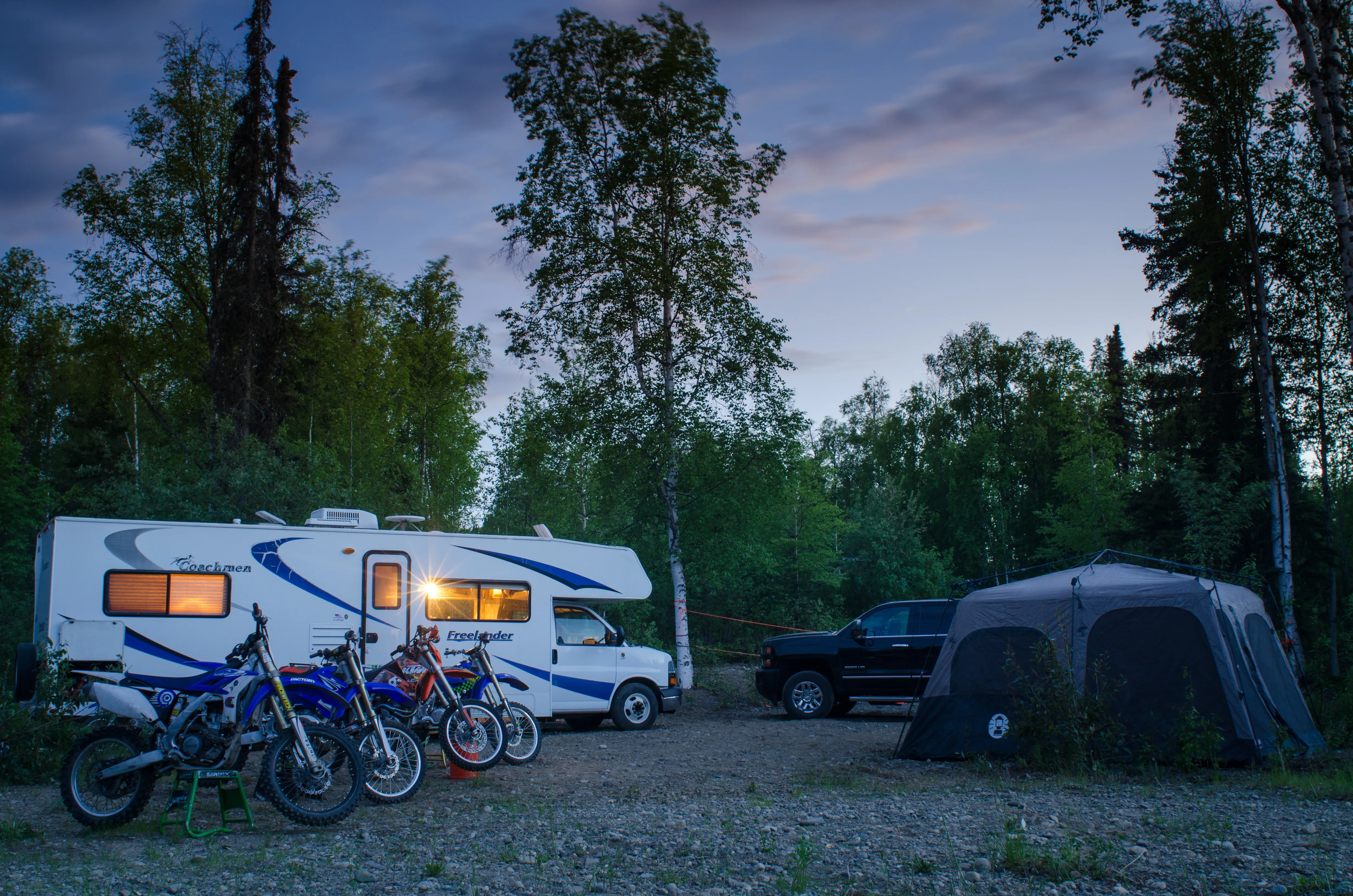 An RV camper is parked next to a tent and several dirt bikes.