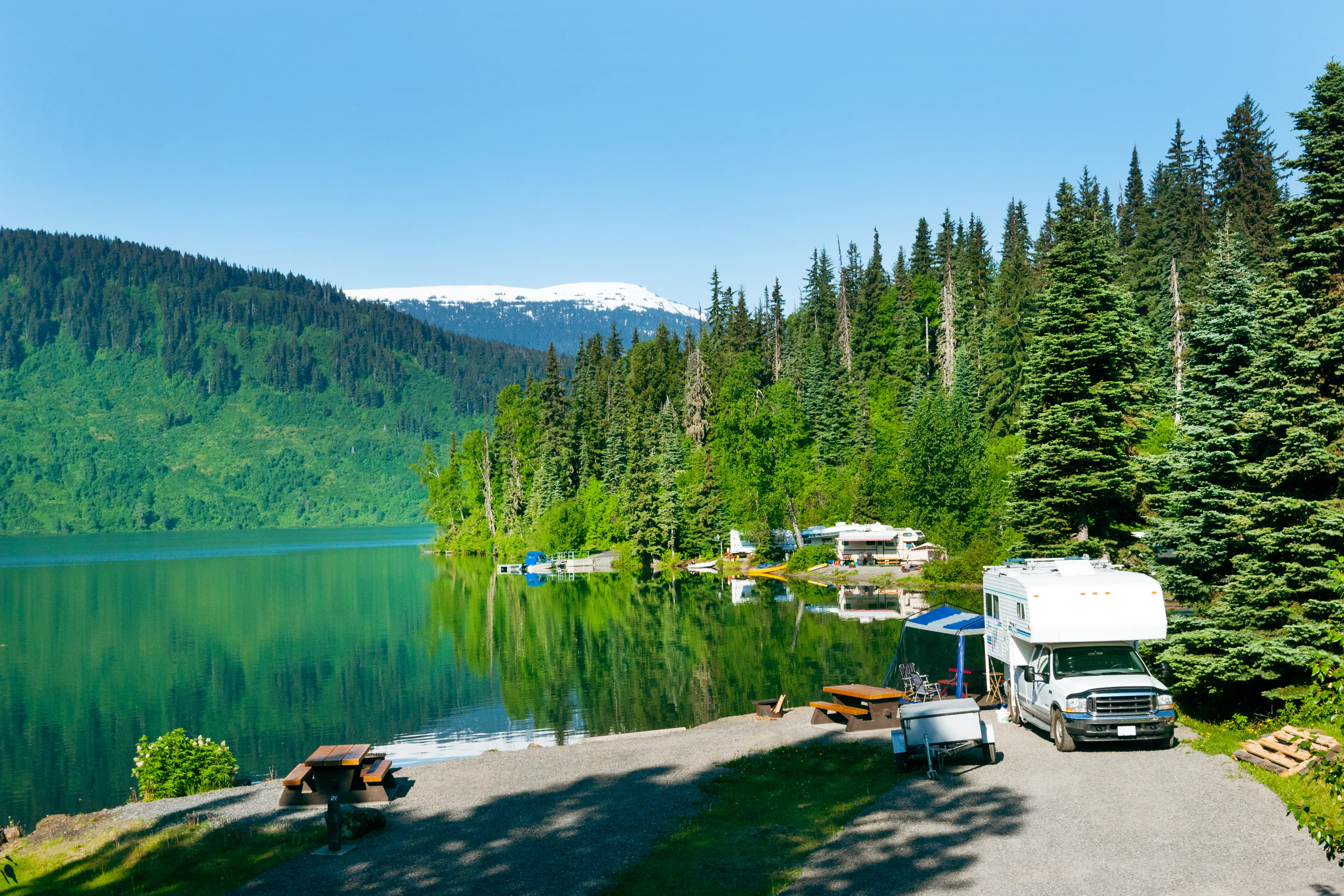 An RV and a small campsite are perched on the edge of a remote and beautiful Alaskan lake.