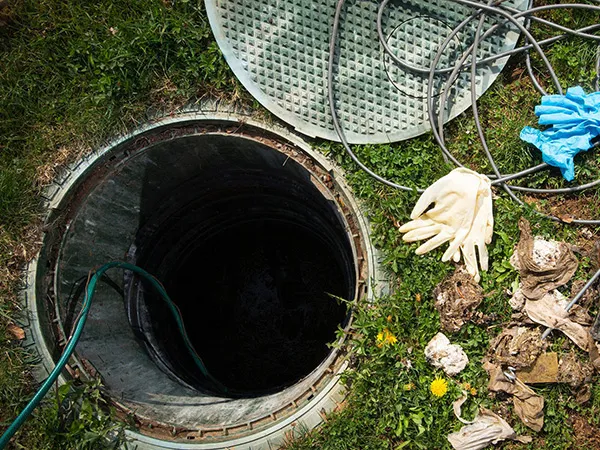 An open septic tank, with gloves and a hose nearby.